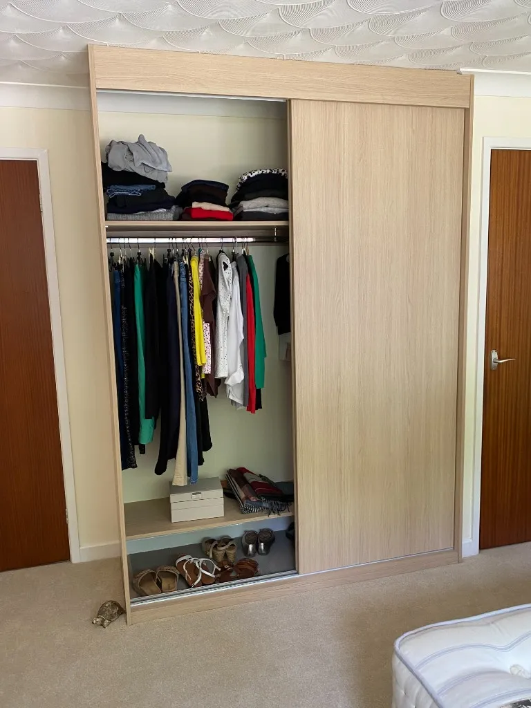 Light oak sliding wardrobe open showing hanging clothes and shelves