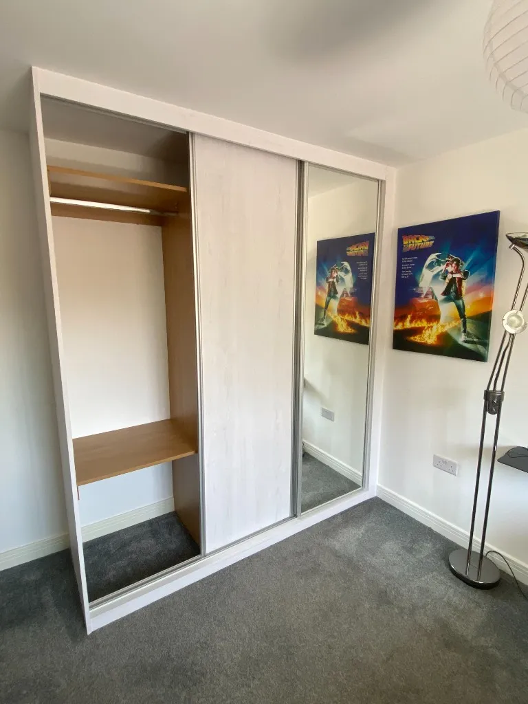 White-frame sliding wardrobe with left bay open showing hanging rail